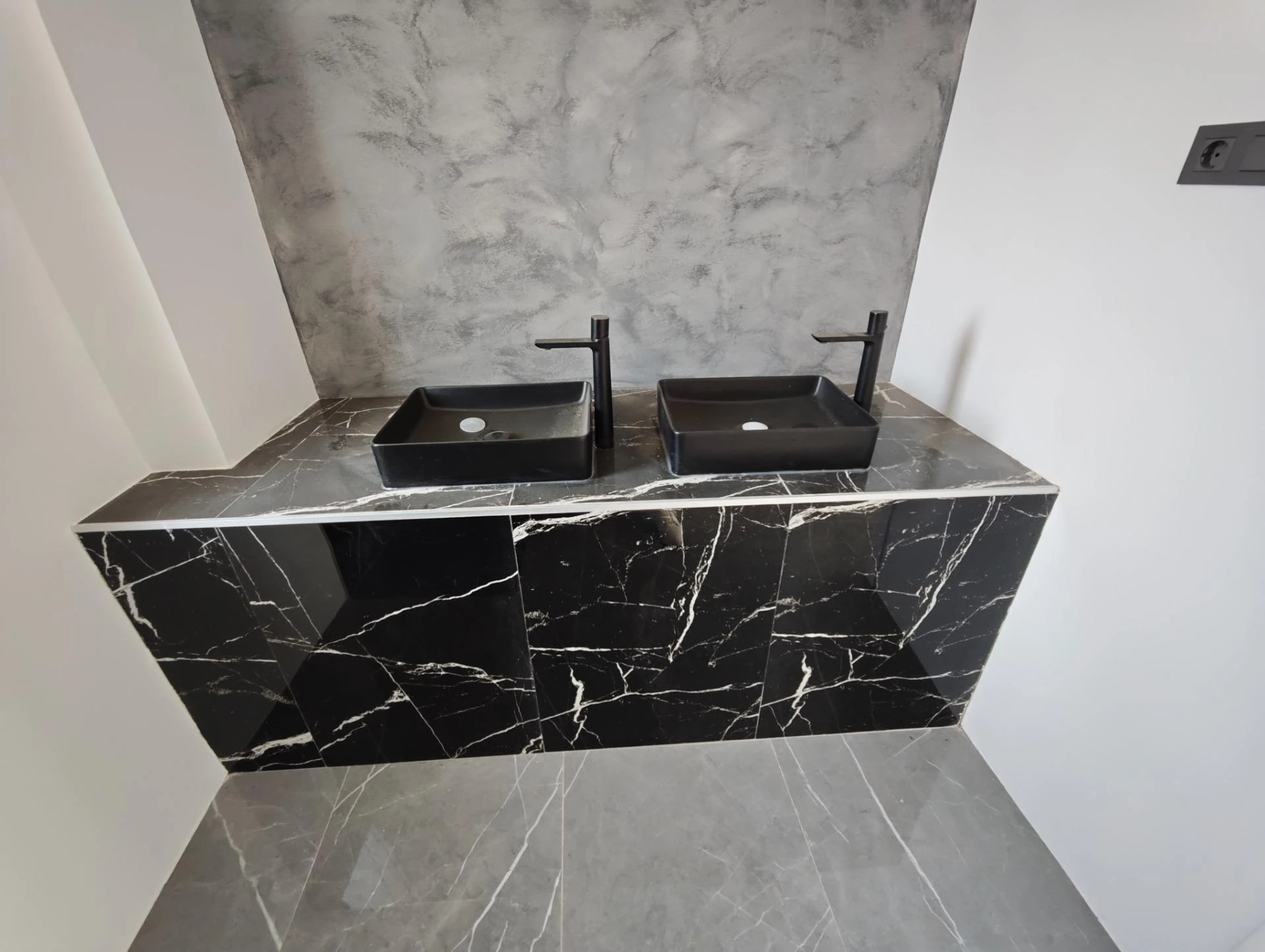 Baño con encimera de mármol negro y doble lavabo